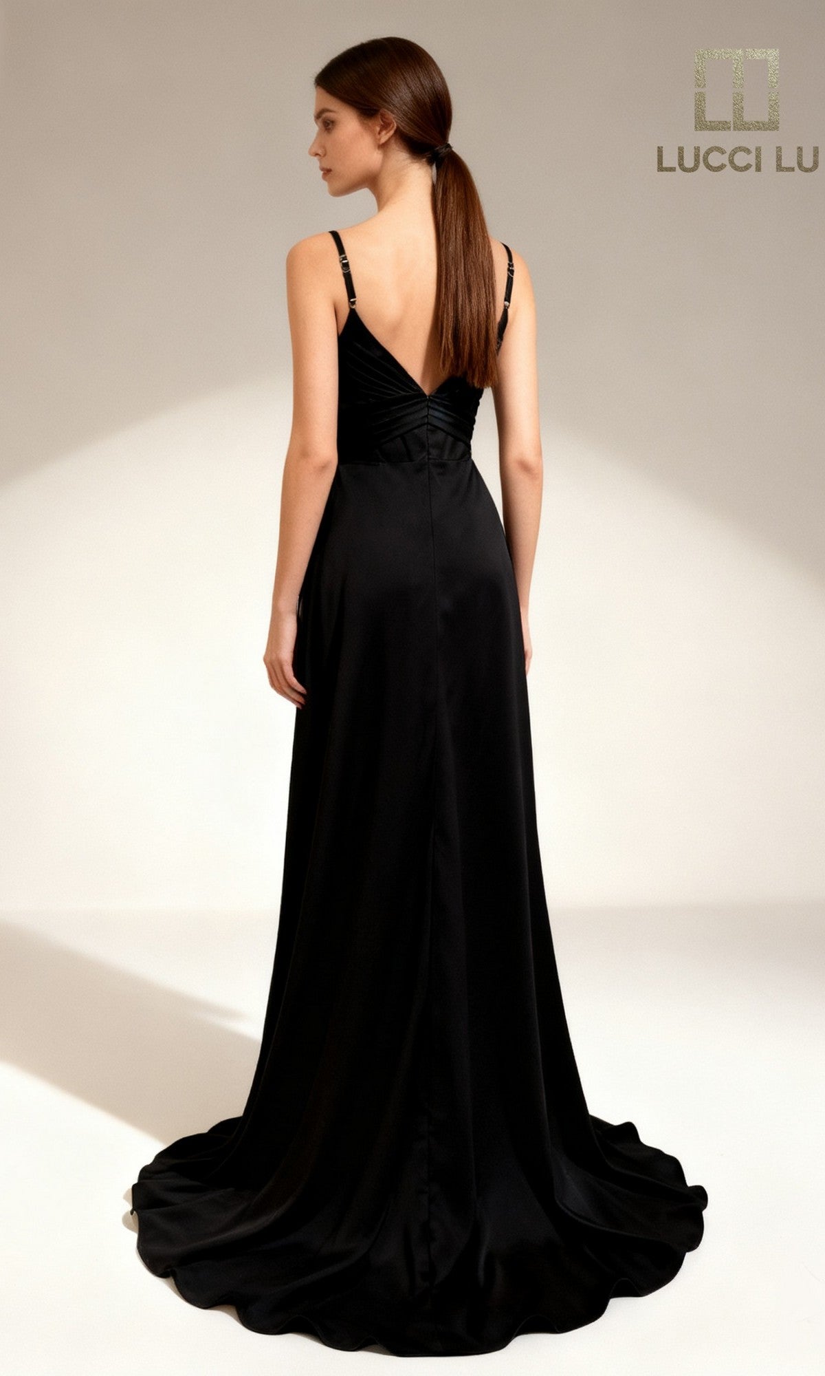 A woman faces away, wearing the Black Abby Paris 90386 long prom dress with a V-back and thin straps, against a plain light background. The Lucci Lu logo appears in the top right corner.